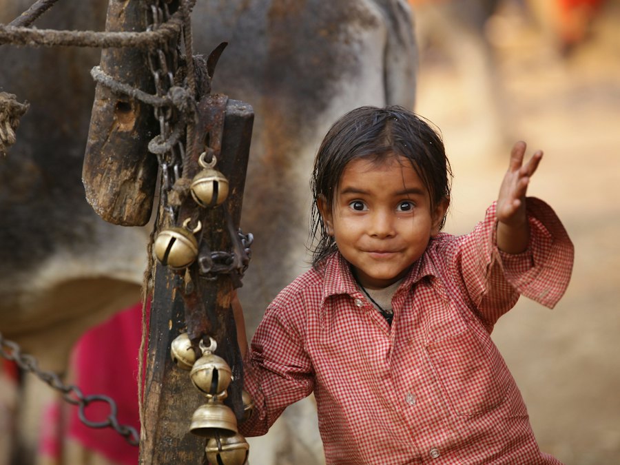 A smiling girl waving next to a cow wearing brass bells